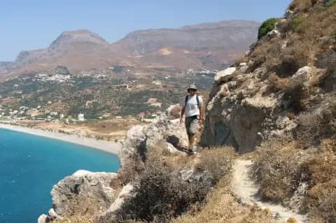 Mann läuft auf einem schmalen, kargen Küstenpfad am Hang entlang hoch über dem blauen Meer