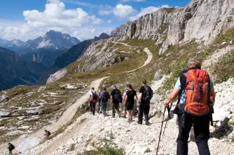 Gruppe von sechs Wanderern läuft Pfad bergab in einer kargen, grünen Berglandschaft unter bewölktem Himmel