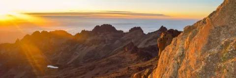 Sonnenaufgang auf einem Berg mit karger Felslandschaft über der Wolkendecke