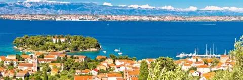 Stadt an der Küste am blauen Meer mit Bergen im Hintergrund unter blauem Himmel