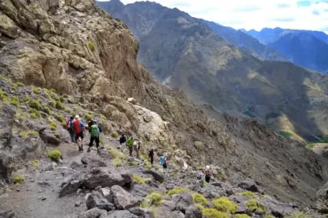 Gruppe von Wanderern läuft Berghang mit Geröll hinauf in einer grauen, felsigen Berglandschaft