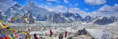 Bergsteiger stehen Neben Gebetsfahnen und blicken auf Bergpanorama mit schneebedeckten Bergen unter blauem Himmel