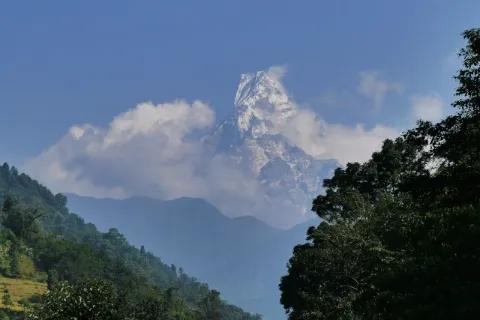 Berg umringt von Wolken unter blauem Himmel und grünen Bäumen im Vordergrund