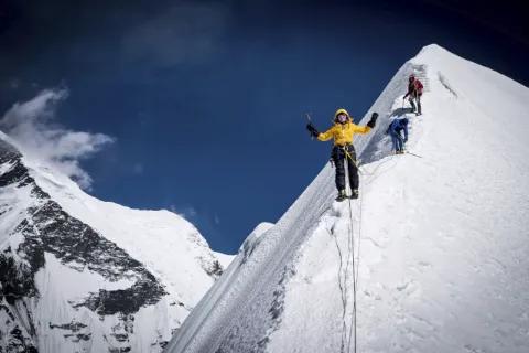 Drei Bergsteiger steigen einen sehr schmalen, schneebedeckten Grat hinauf, umringt von schneebedeckten Berge.