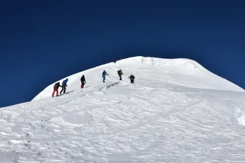 Sechs Bergsteiger mit Rucksack laufen schneebedeckten Berghang hoch unter blauem Himmel
