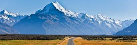 Straße führt auf eine schneebedeckte Bergkette zu mit einem hohen Berg in der Mitte