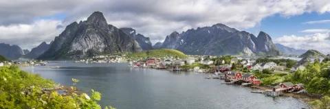 Dorf mit roten Häusern am Rand eines Fjords mit hohen Bergen im Hintergrund