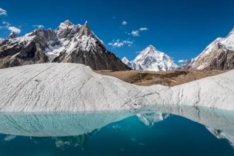 Ein türkiser Gletschersee umgeben von weißen Gletschern. In der Ferne sind schneebedeckte Berge.