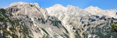 Eine Bergkette aus grauen Stein. Teils sind die Berge von grünen Büschen und Rasen bewachsen.
