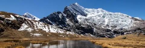 Schneebedeckte Berge hinter einer Lagune mit dunklem Wasser und brauner Wiese an den Seiten