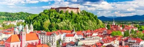 Luftaufnahme einer Stadt mit weißen Häusern und roten Dächern und einem grünen Hügel mit einem Schloss