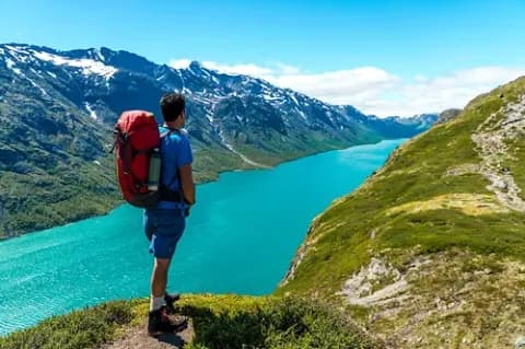 Ein Mann mit Wanderrucksack auf dem Rücken blickt vom Besseggen auf den Gjende-See in Norwegen.
