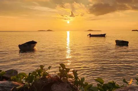 Drei Boote schwimmen auf dem Wasser, die Sonne geht über dem Horizont unter.