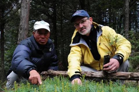 Zwei Männer sitzen auf einer Wiese mit Baumsetzlingen