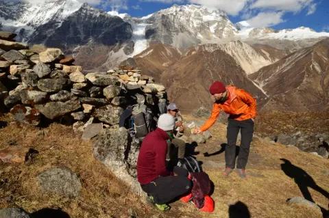 Ein Wanderer beugt sich zu zwei sitzenden Menschen und teilt Snacks