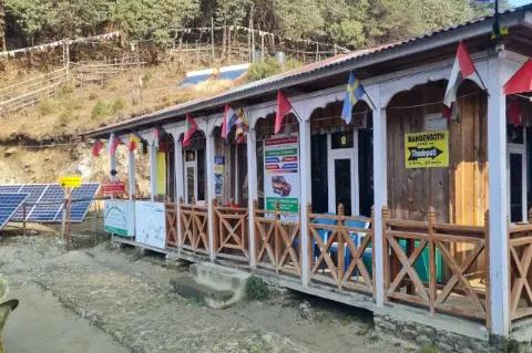 Blick auf eine Holz-Lodge mit internationalen Fahnen. Neben der Lodge stehen Solarpanele und auf einem Hügel Solar-Wassererhitzer.