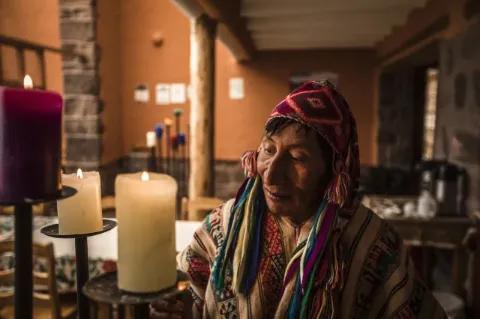 Ein Mann in traditioneller bunter Kleidung der Region steht vor drei großen, brennenden Kerzen.