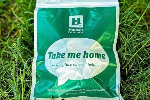Auf dem Gras liegt ein Grün-weißer Beutel mit dem Firmenlogo und dem Begriff take-me-home