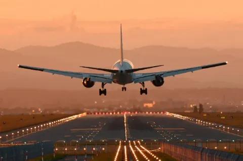 Es ist ein Flugzeug von hinten zu sehen, das im Abendlicht auf einer Landebahn landet.