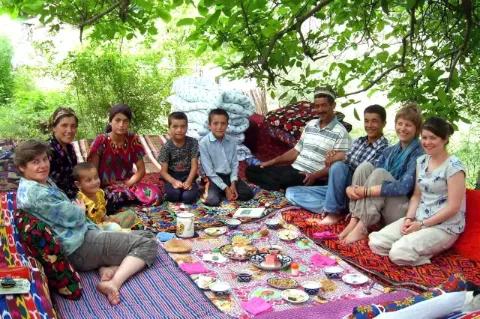 Eine diverse Gruppe sitzt am Boden um eine Picknickdecke herum. Auf der Decke ist Geschirr und Essen vorbereitet.