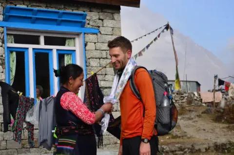 Eine nepalesische Frau begrüsst einen Wanderer mit einem typisch nepalesischen Schal, den sie ihm um den Hals legt.