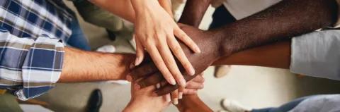 Blick von oben auf einen Kreis von Menschen, die in der Mitte ihre Hände aufeinander legen