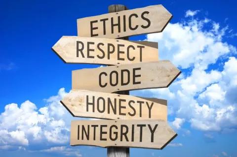 Vor einem blauen Hintergrund steht ein Wegweiser aus Holz mit beschrifteten Schildern. Die abgebildeten Begriffe lauten: Ethik, Respekt, Kodex, Ehrlichkeit, Integrität