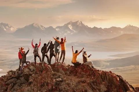 Eine große Gruppe glücklicher Touristen hat Spaß und begrüßt den Sonnenuntergang auf dem Berggipfel.