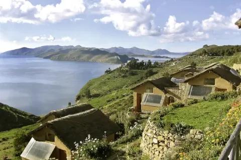 Blick über mehrere Holzhäuschen an einem Hang. Im Hintergrund ist eine blaue Bucht zu sehen.