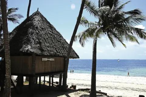 Eine runde Hütte auf Stelzen steht an einem Strand. Neben der Hütte steht eine Palme und im Hintergrund ist das Meer zu sehen.