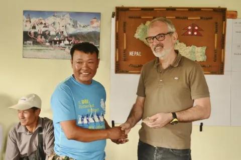 Zwei Menschen stehen vor einer gelben Wand und geben sich die Hand.