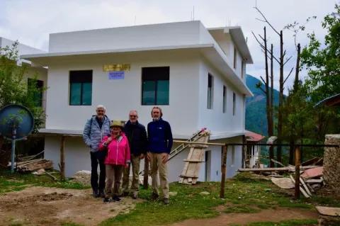 Vier Personen stehen vor einem kleinen, weiß gestrichenen Haus und lachen in die Kamera.