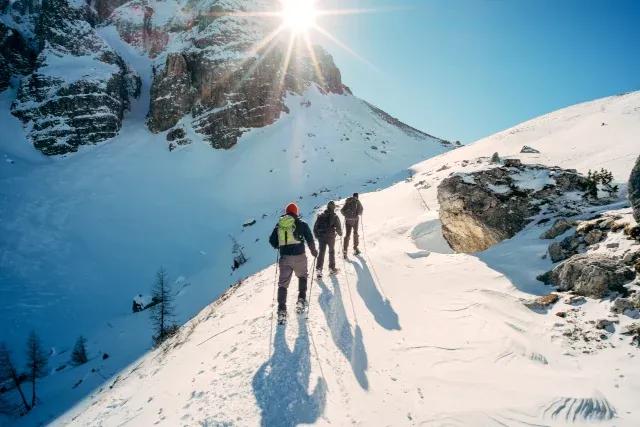 Drei Wanderer laufen verschneiten Berghang bei Sonnenschein und blauem Himmel hinauf