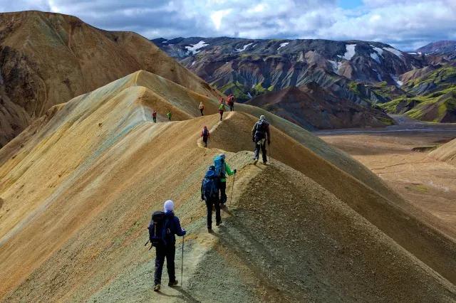 Trekkinggruppe läuft bei bewölktem Himmel über die Berge auf einem schmalen Grat