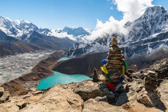 Blick vom Gipfel auf einen blauen See im Tal und vielen schneebedeckten Bergen im Hintergrund.