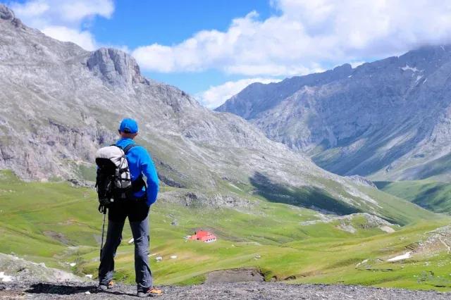 Wanderer mit Rucksack blick auf eine Bergkulisse mit grünen Wiesen und grauen Bergen