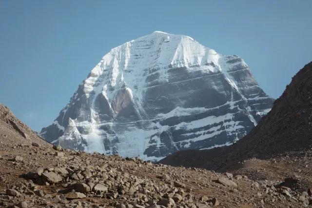 Von einem braunen, gerölligen Berg schaut der Fotograf auf einen schneebedeckten Gipfel.
