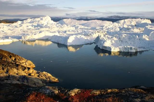 In einem Eisfjord fließt das Wasser. Auf der einen Seite ist der Fjord Felsig, auf der anderen Seite aus Eis.