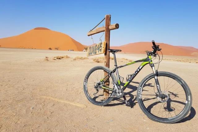 Ein Mountainbike Fahrrad lehnt an einem Schild, auf dem "Dune 45" steht. Dahinter ist eine große Düne.