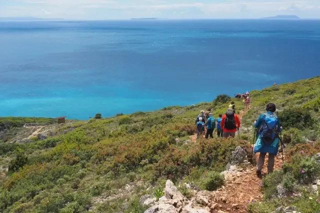 Gruppe von Wanderern laufen an der Küste bergab in Richtung Strand mit Blick auf das blaue Meer
