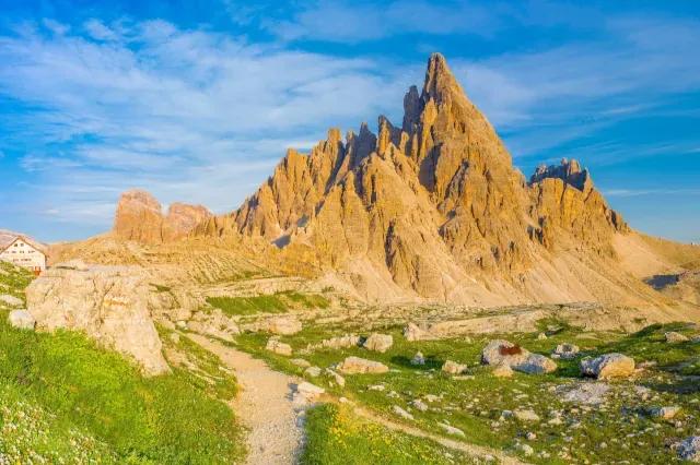 Wanderweg führt vorbei an Wiesen auf Berge im Abendlicht zu unter leicht bewölktem Himmel