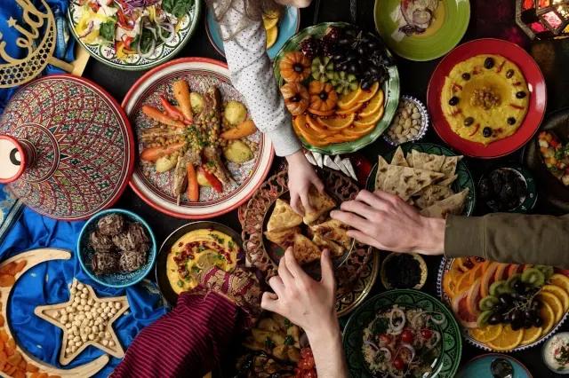 Verschiedenes orientalisches Essen ist auf bunten Tellern und Schüsseln angerichtet. Verschiedene Hände greifen zu Teigtaschen in der Mitte der Tisches.