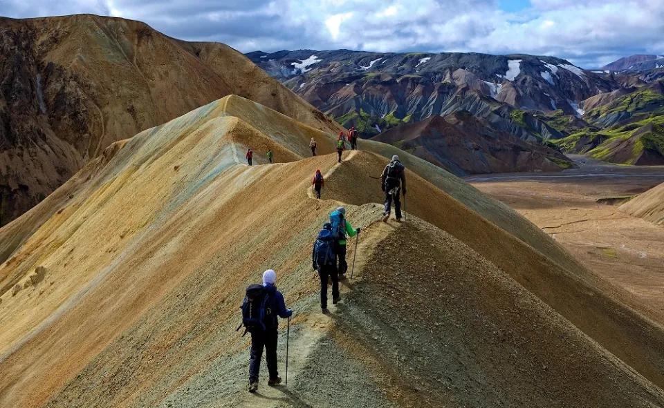 Trekkinggruppe läuft bei bewölktem Himmel über die Berge auf einem schmalen Grat