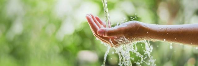 Wasser strömt auf die Hand der Frau auf Naturhintergrund