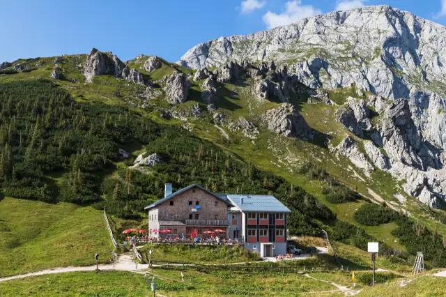 Kleine Berghütte steht am Fuße Berghangs mit Wald und Felsen im Hintergrund