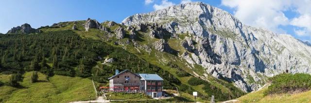 Kleine Berghütte steht am Fuße Berghangs mit Wald und Felsen im Hintergrund