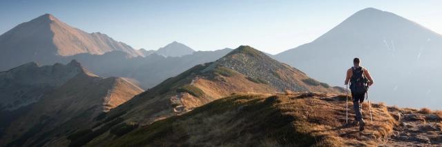 Ein Wanderer mit Rucksack und Wanderstöcken geht auf einem Pfad auf einem Grad in den Bergen