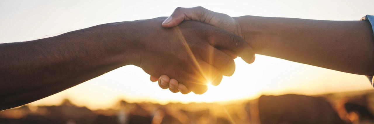 Zwei Hände umfassen sich vor einem warmen Hintergrund mit Sonnenstrahlen
