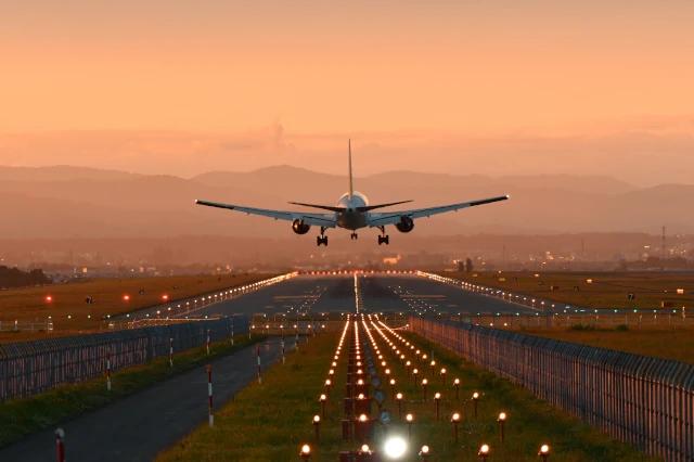 Flugzeug hebt auf beleuchteter Landebahn ab in einer orangenen Lichtstimmung am Abend