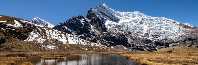 Schneebedeckte Berge hinter einer Lagune mit dunklem Wasser und brauner Wiese an den Seiten